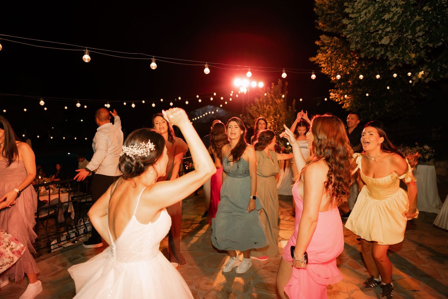 People dancing together outdoors at night under string lights during a festive celebration.