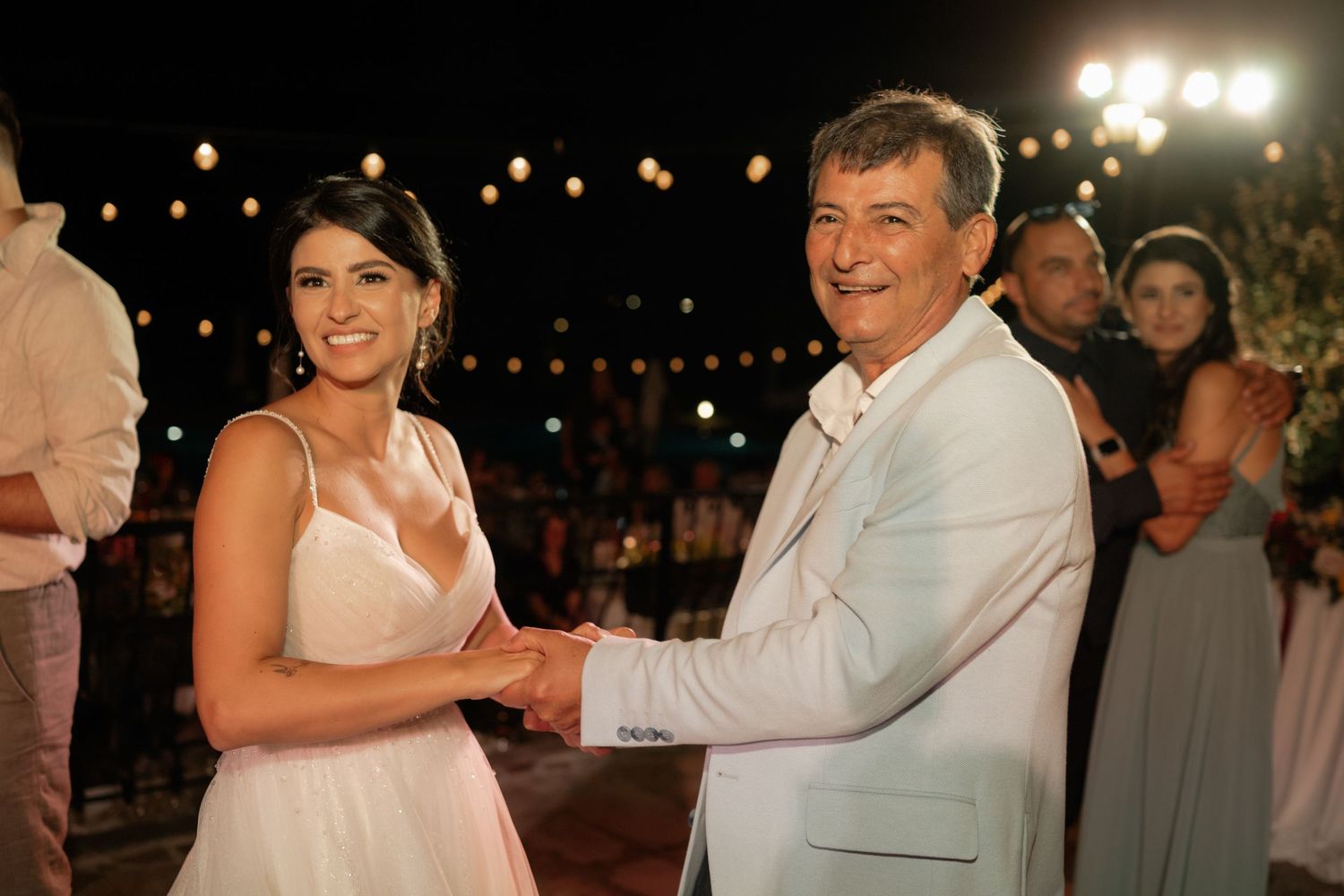 Couples dance together at an outdoor evening wedding reception under string lights and glowing lanterns.