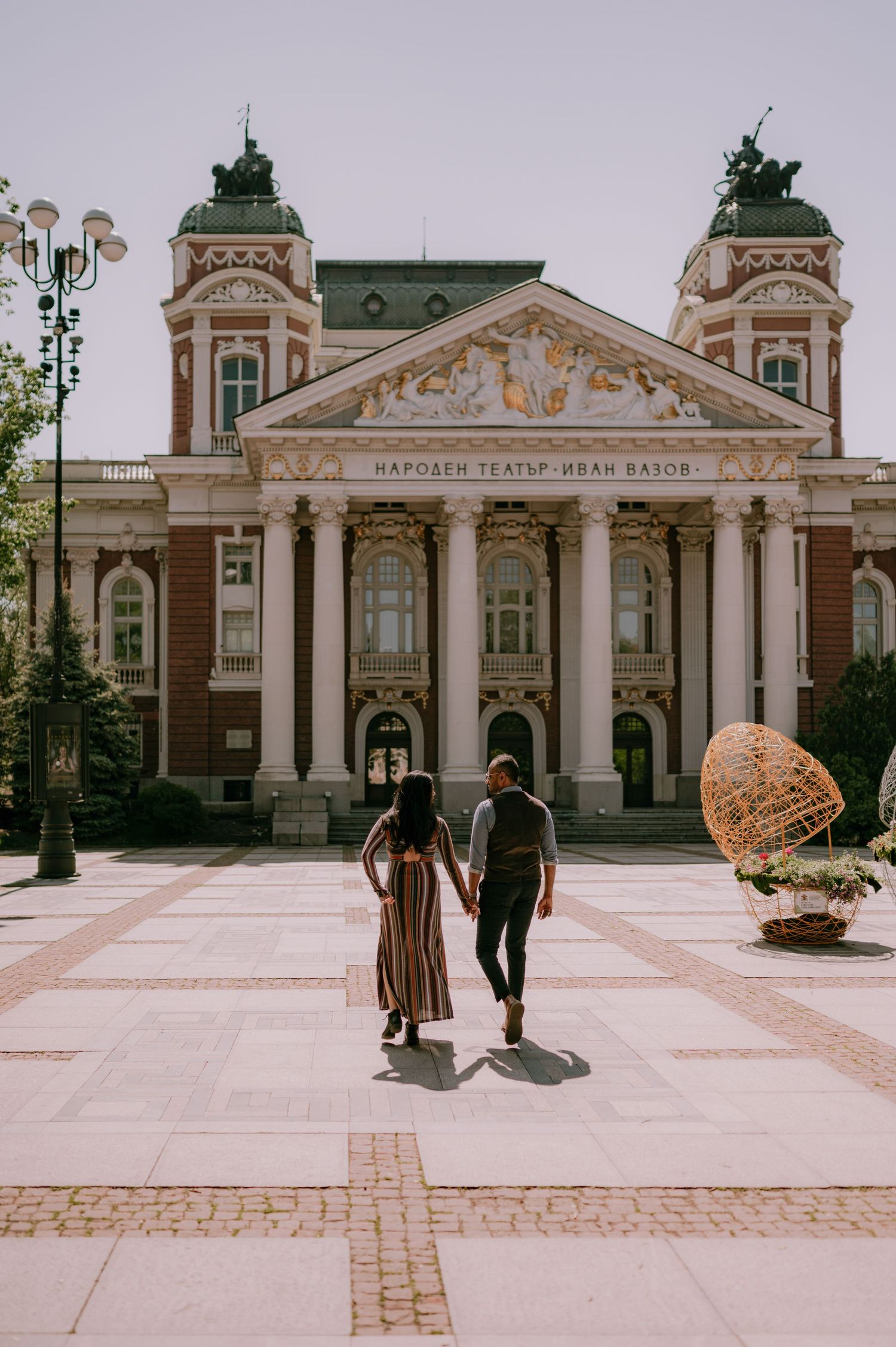 Couple walking hand in hand toward the Ivan Vazov National Theatre in Sofia, Bulgaria.