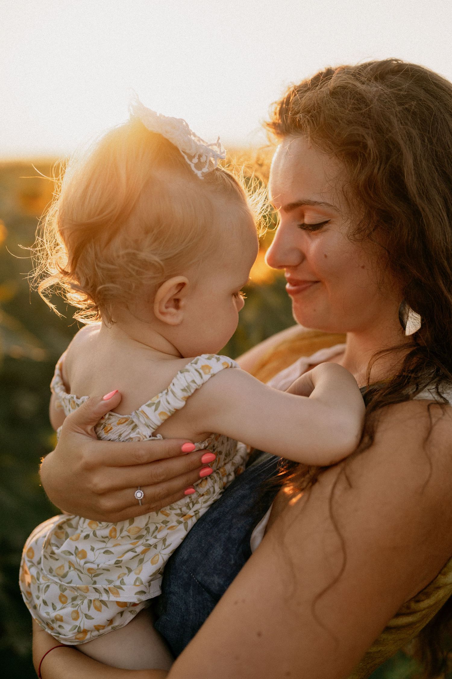 A mother tenderly holds her baby in a sunlit field, sharing a sweet moment at golden hour.