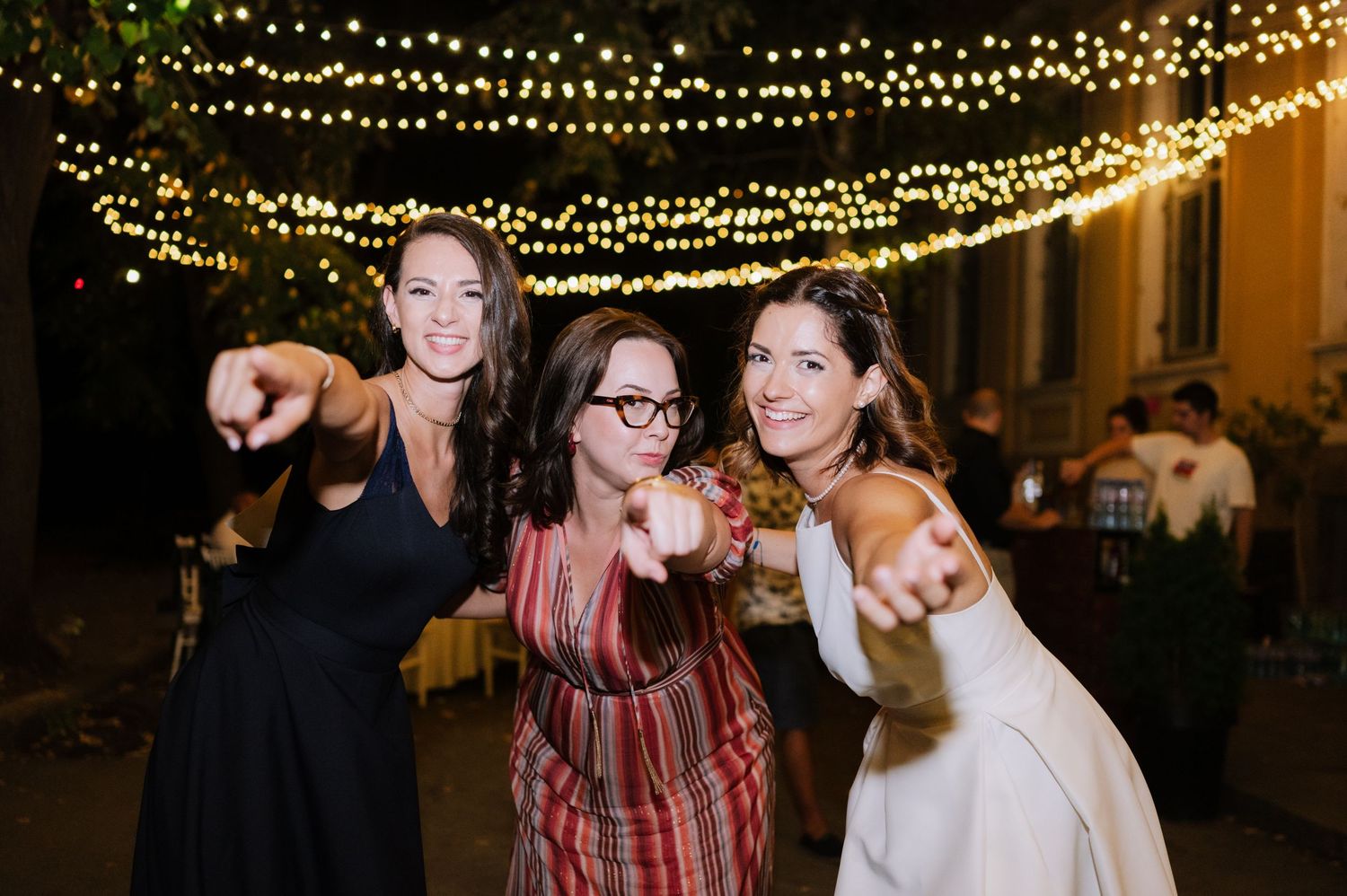 Wedding guests celebrate under twinkling string lights at an outdoor evening reception.