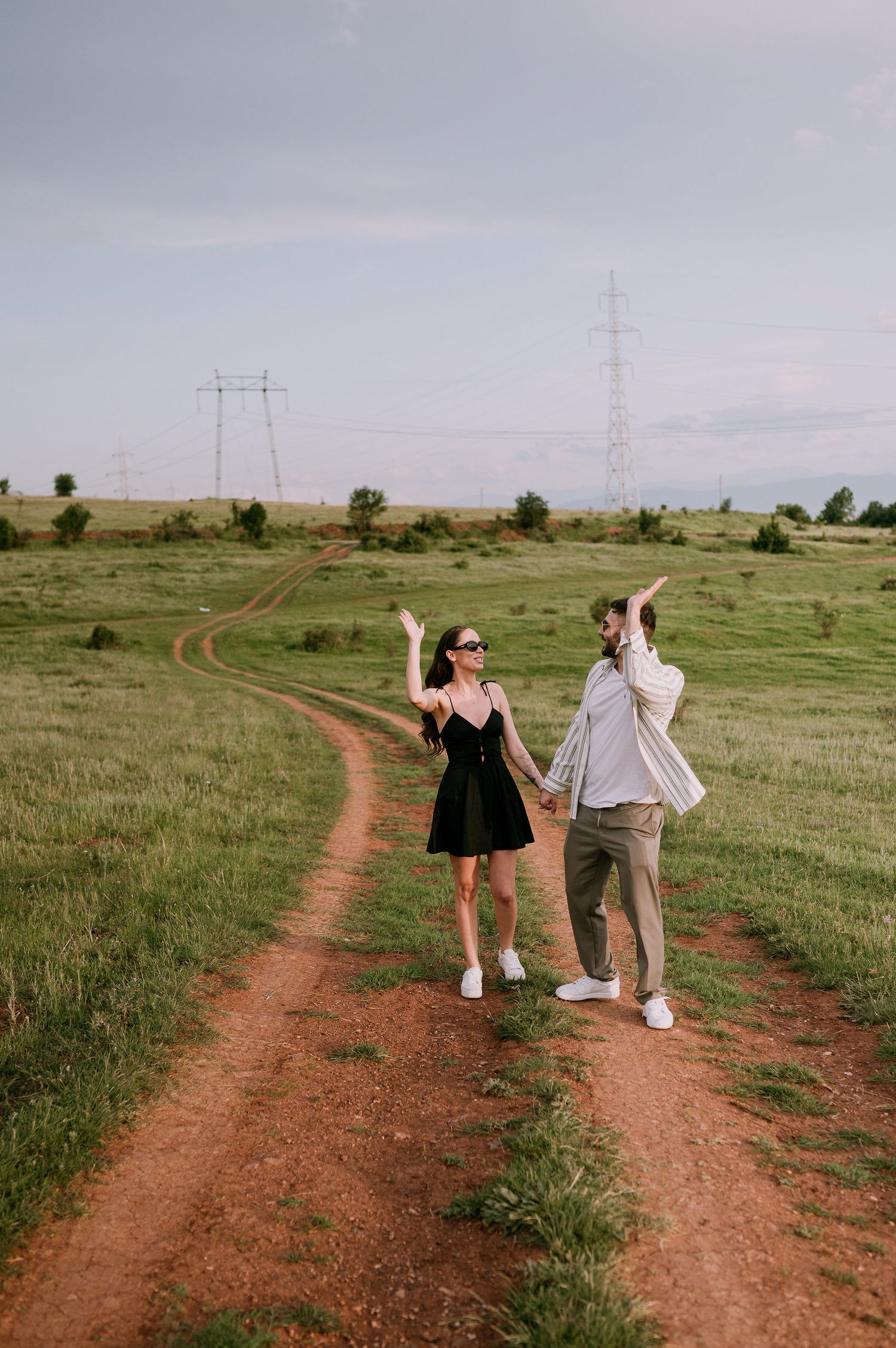 A group walks along a winding dirt path through a grassy field with power lines in the distance.