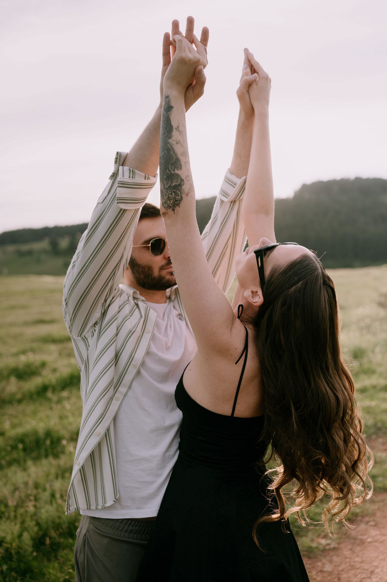 A couple dances together in a meadow at sunset, holding hands raised in joyful celebration.