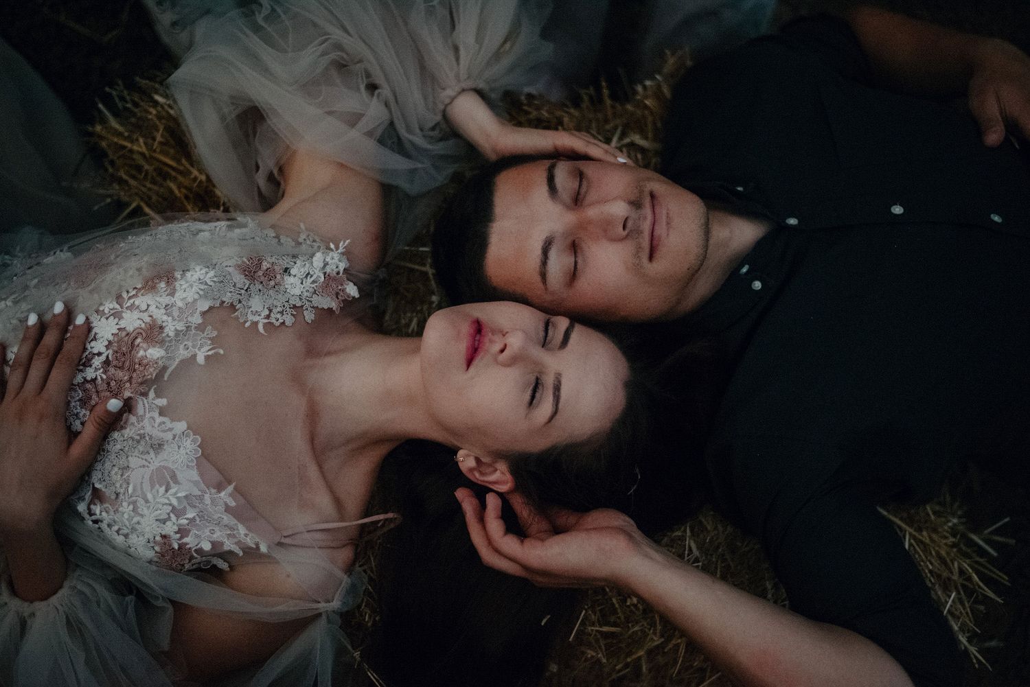 A dark and moody portrait photoshoot with a person lying down against a black background with delicate white floral elements.
