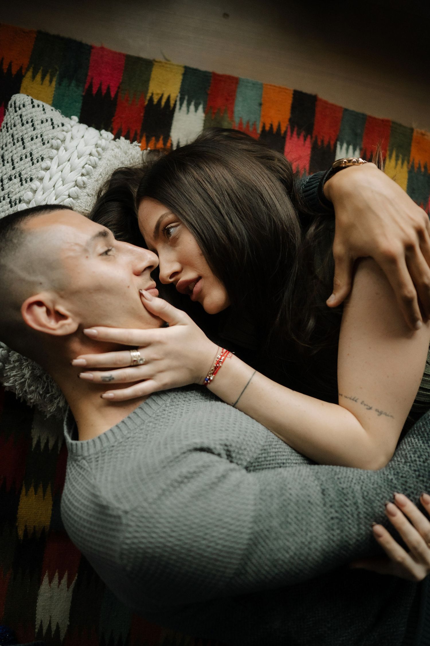 Intimate couple embraces on colorful patterned blanket as they share a tender romantic moment together.