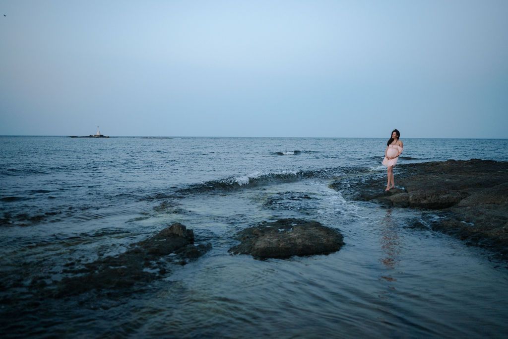 A serene coastal landscape with dark rocky outcrops extending into the misty blue ocean at dusk.