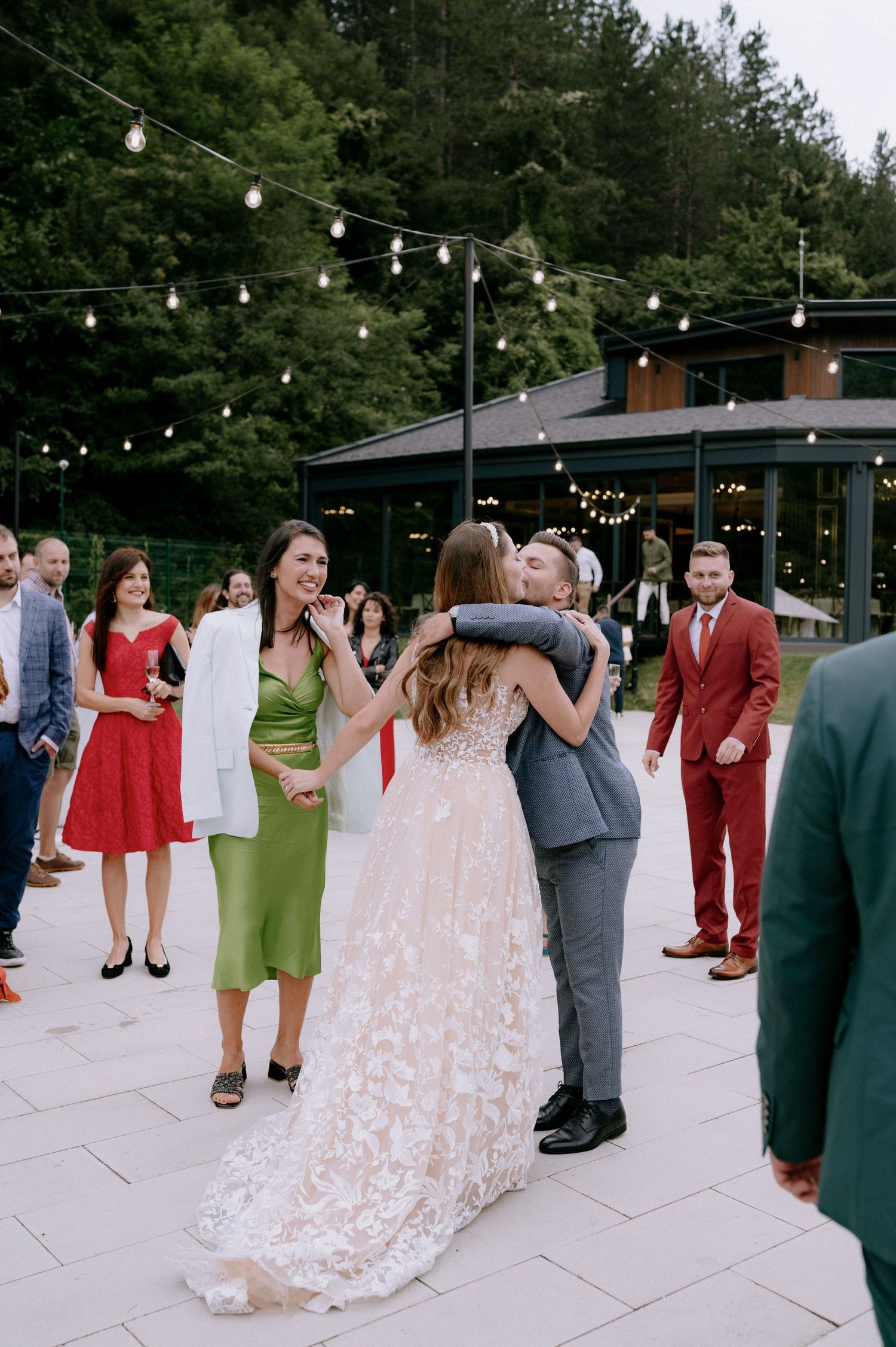 Wedding guests dancing outdoors on a patio under string lights during an evening reception celebration.