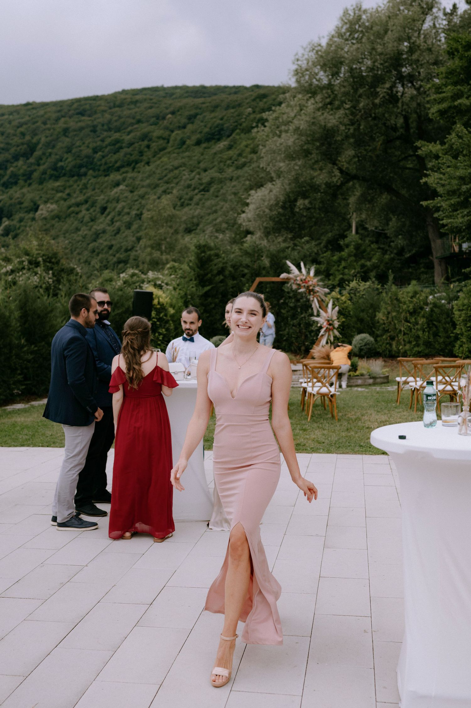 Wedding guests mingle and dance on an elegant white dance floor surrounded by lush green mountains and forest scenery.
