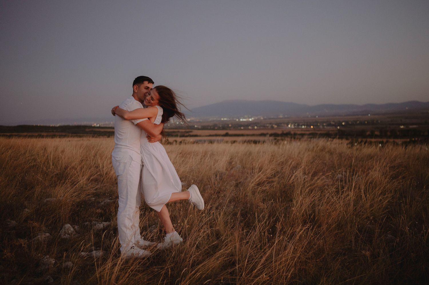Romantic couple embraces in golden wheat field at sunset creating silhouette against warm sky.