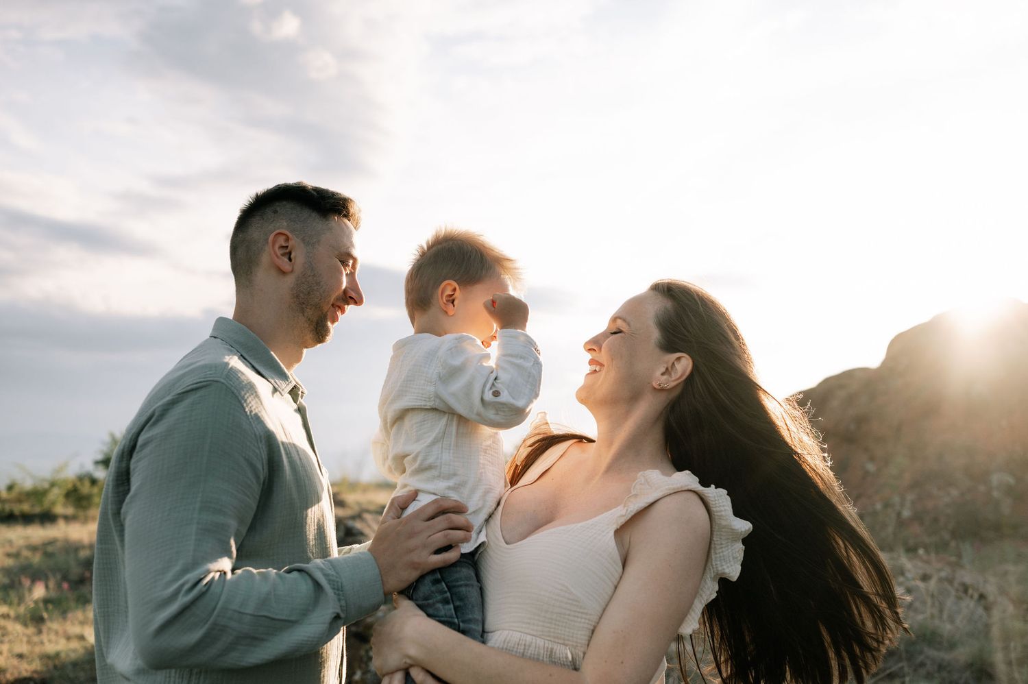 A family shares a joyful moment together outdoors during golden hour with sunlight streaming behind them.