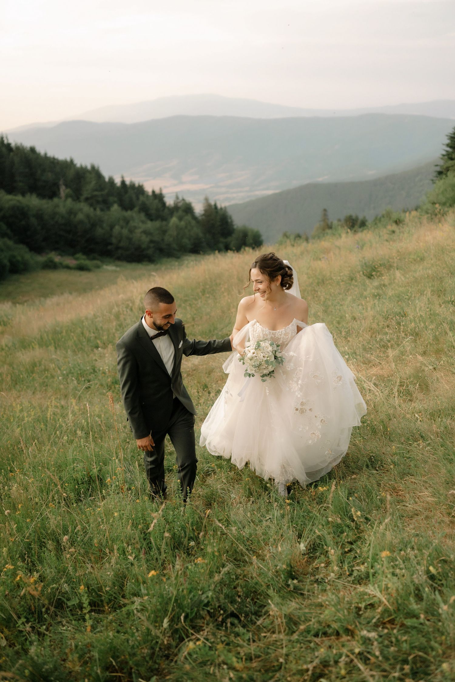A couple strolls through a wildflower meadow with mountain vistas in the background during their wedding.
