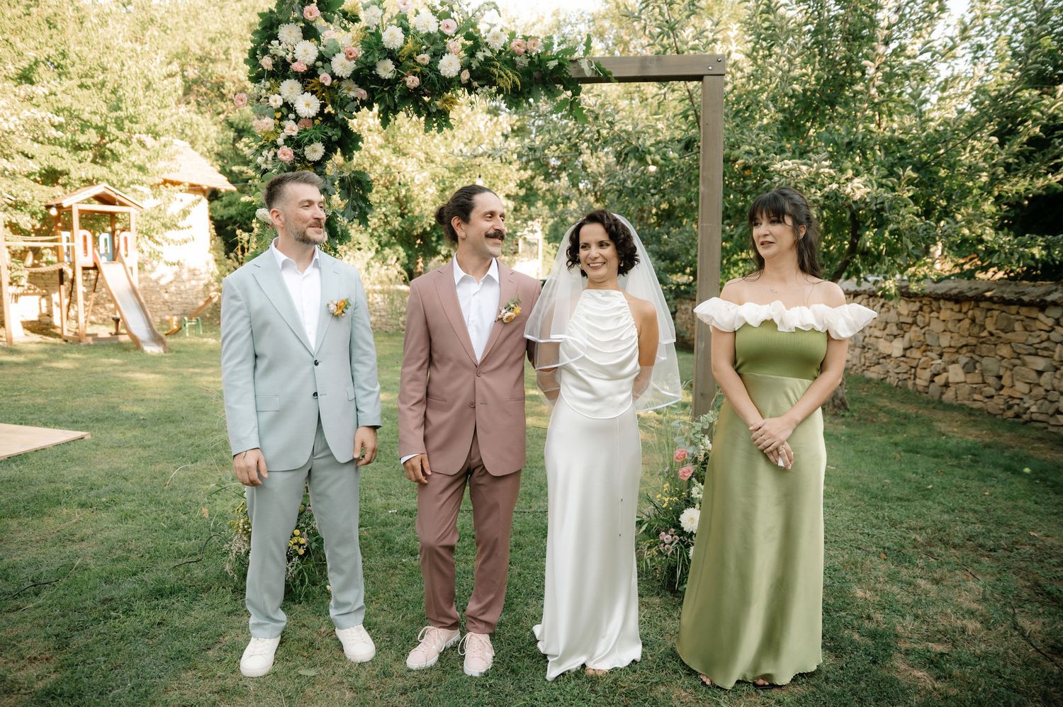 A wedding party poses in pastel colored attire on a sunny lawn during an outdoor summer celebration.