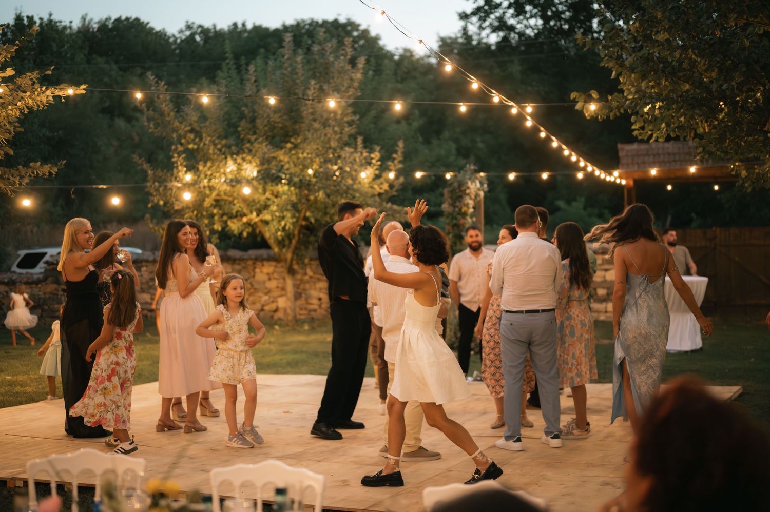 People dancing outdoors under warm string lights at a rustic evening celebration.