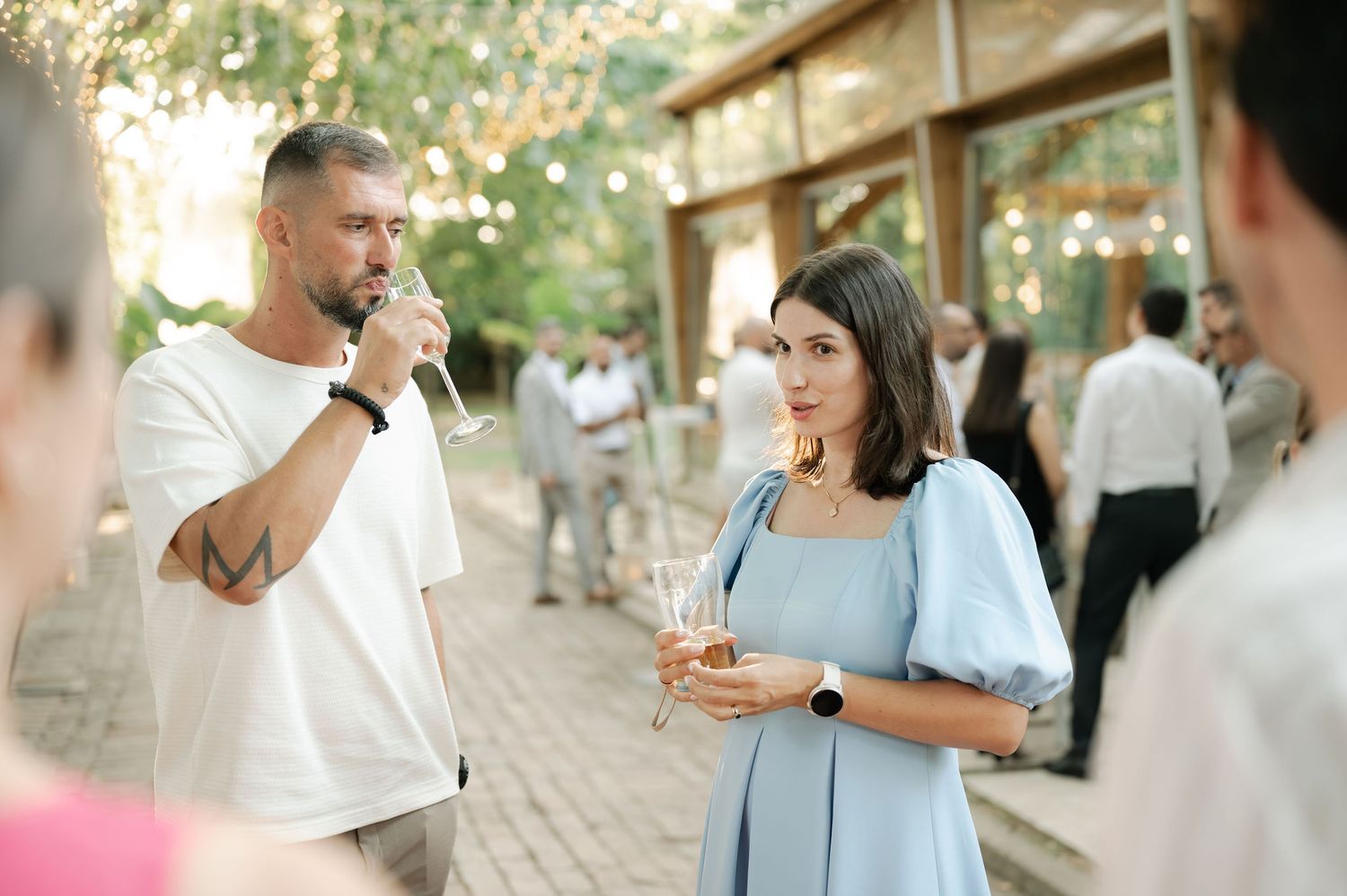 Two people having an animated conversation while holding drinks at an outdoor social gathering.