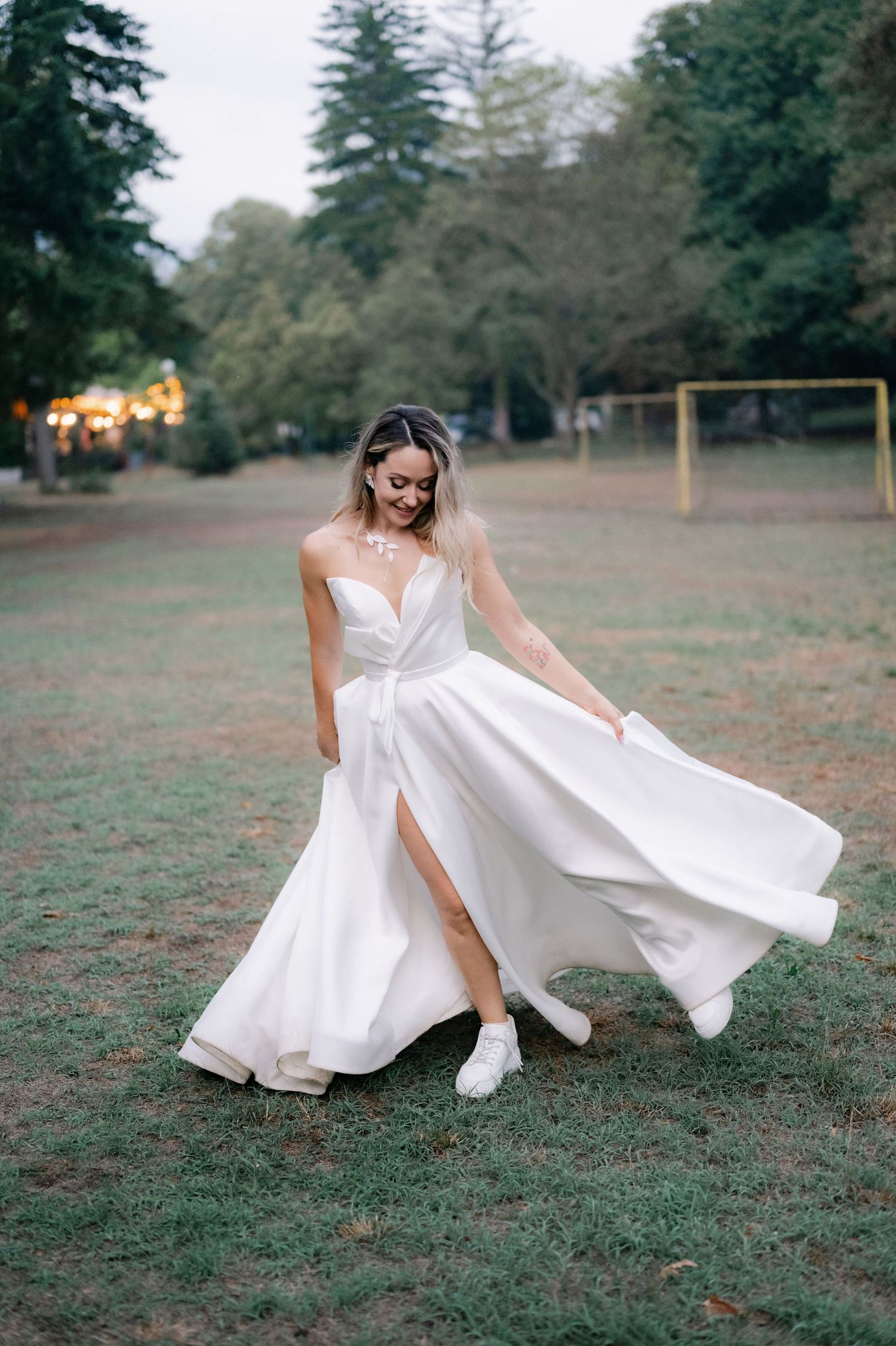 A graceful figure in a flowing white wedding dress twirls playfully in a grassy field at dusk.