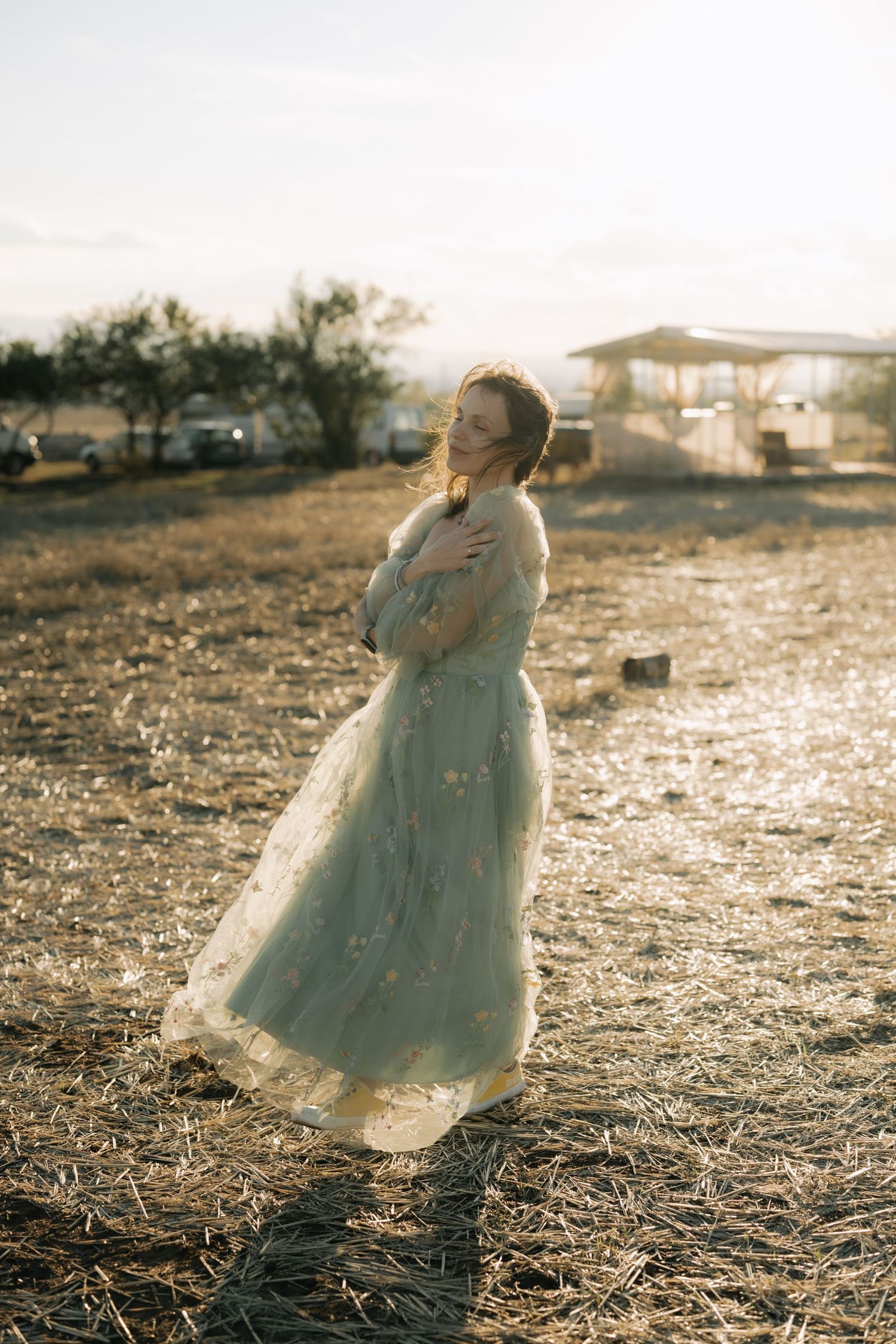A person in a flowing white vintage dress stands in a sunlit field at golden hour with a dreamy, ethereal atmosphere.
