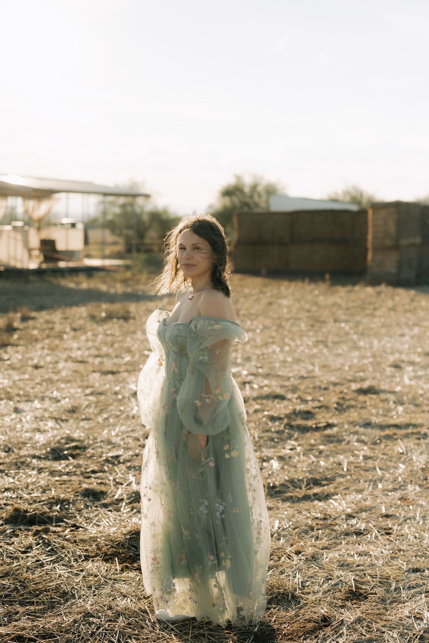 A person in a flowy white dress stands in a sunlit field at golden hour creating an ethereal silhouette.