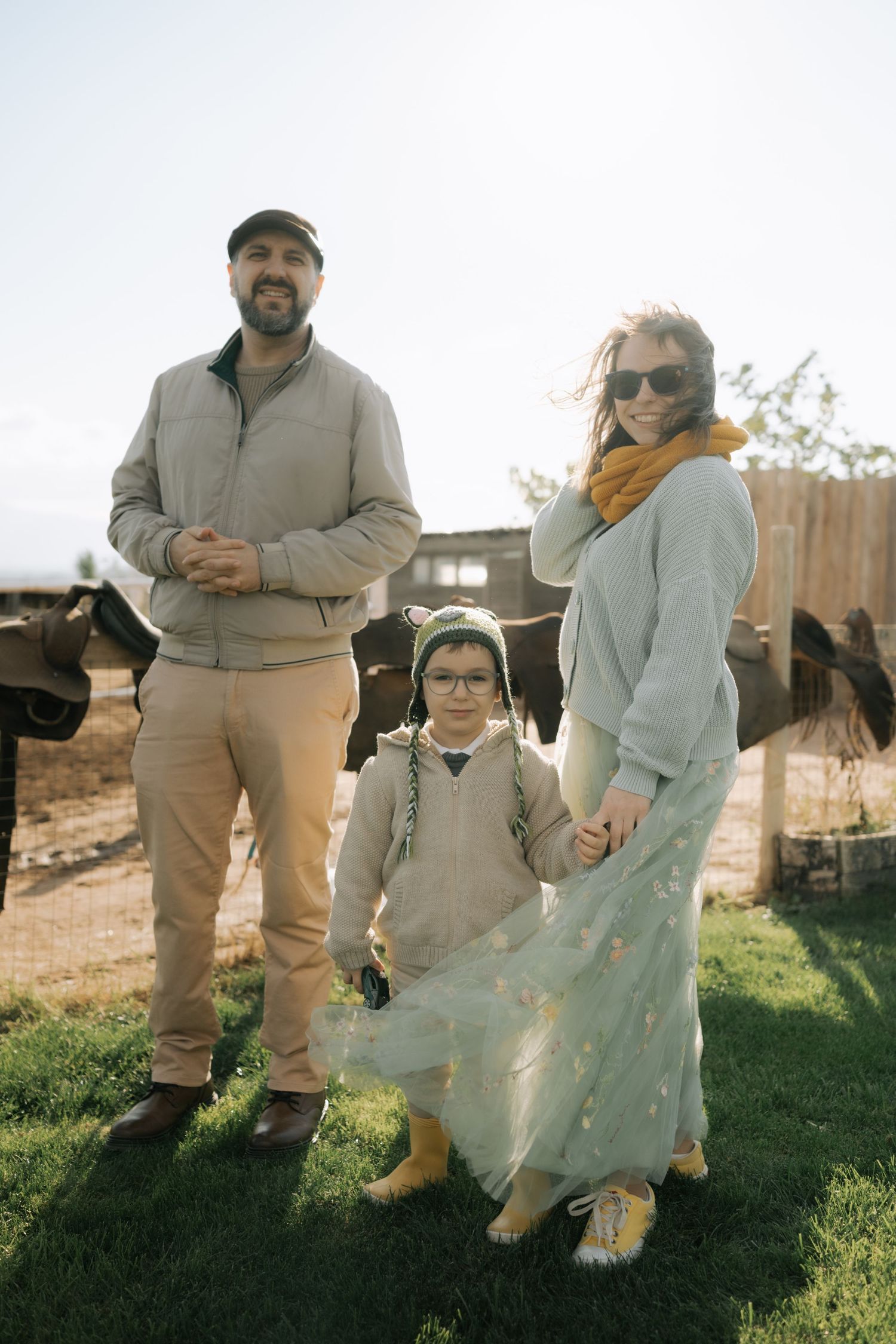 A family poses together on a grassy hillside wearing matching beige and cream colored outfits in autumn light.