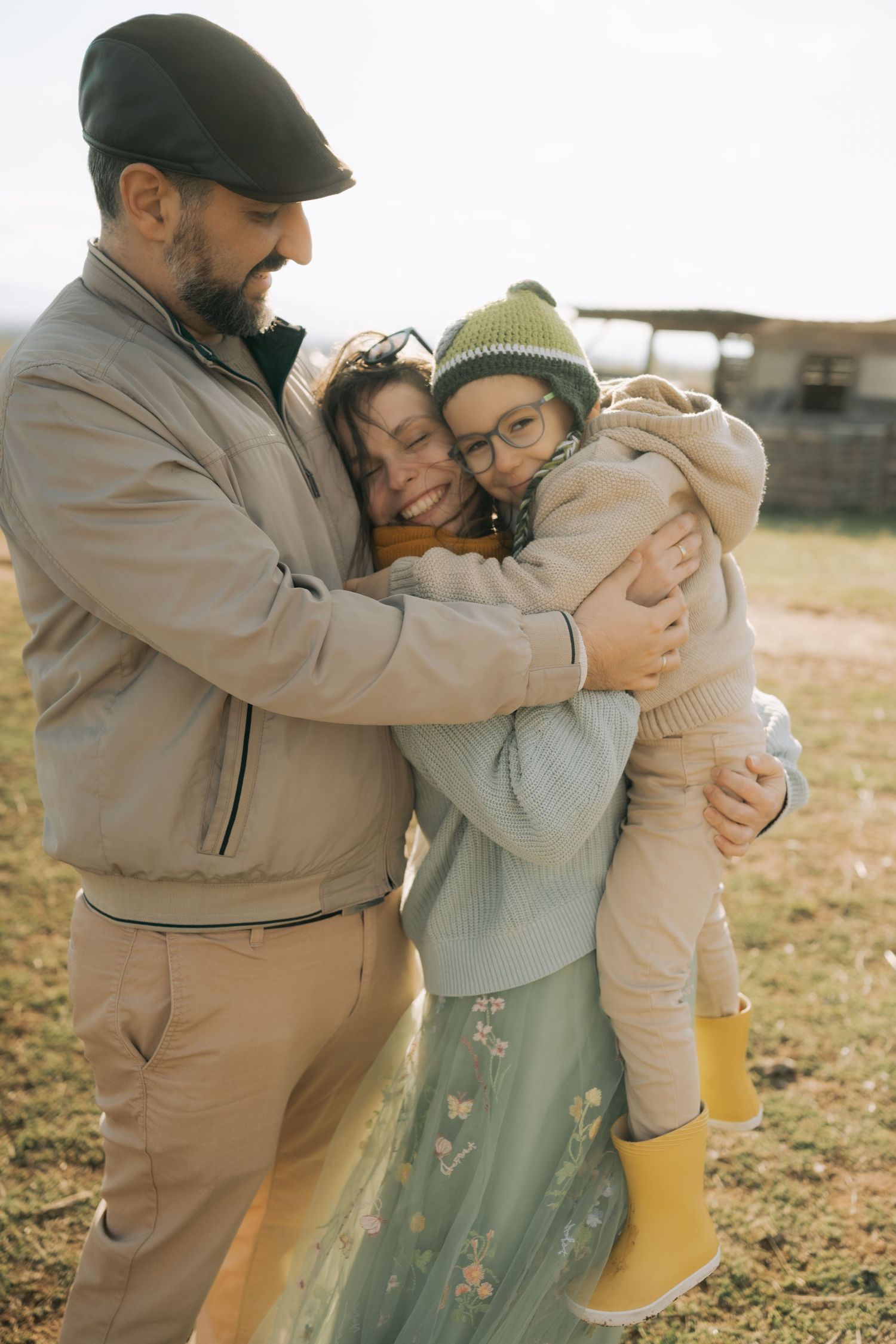 A tender family moment captured outdoors as they share a group hug while wearing casual winter clothing.