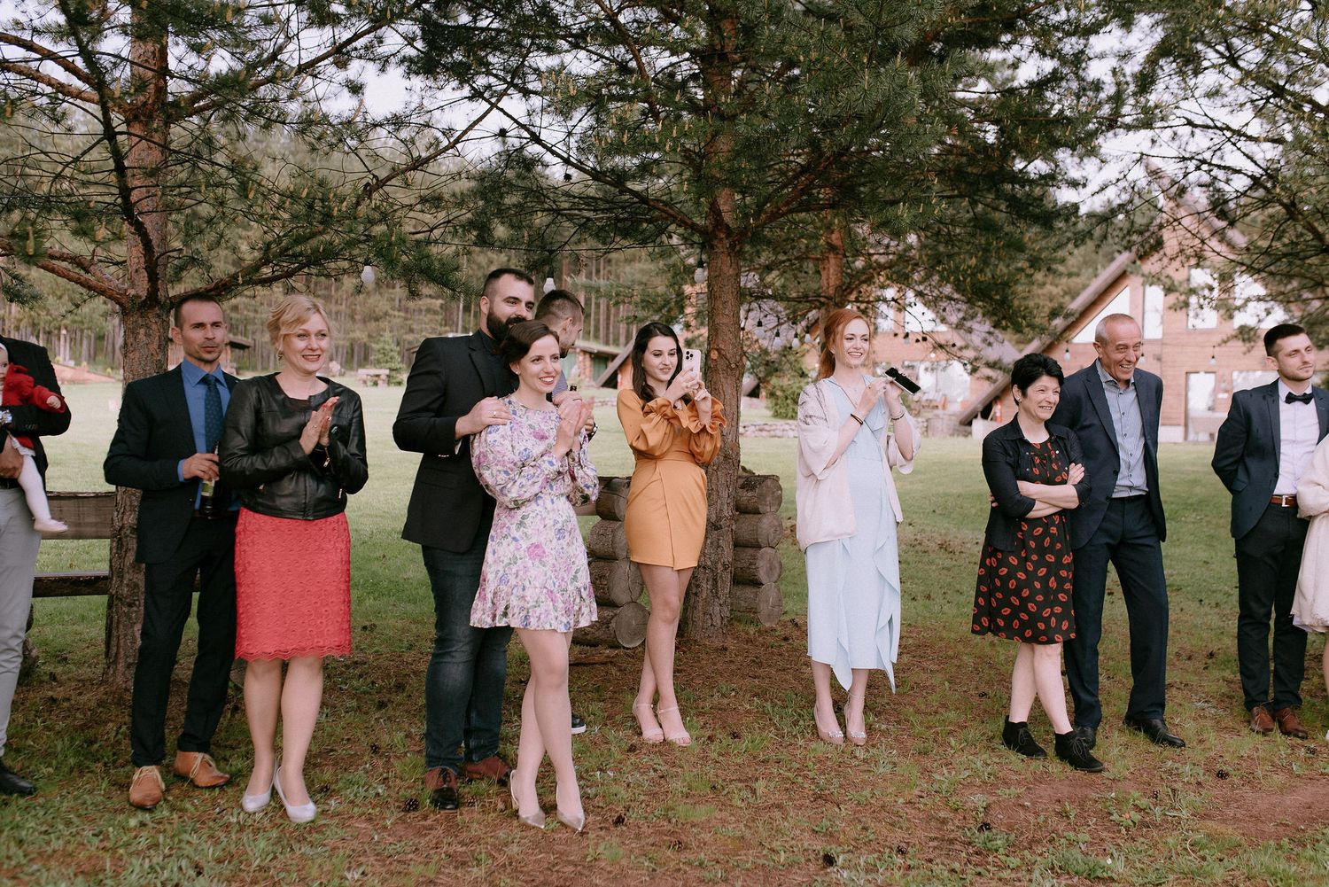 Wedding guests stand in a line against a natural wooded backdrop.