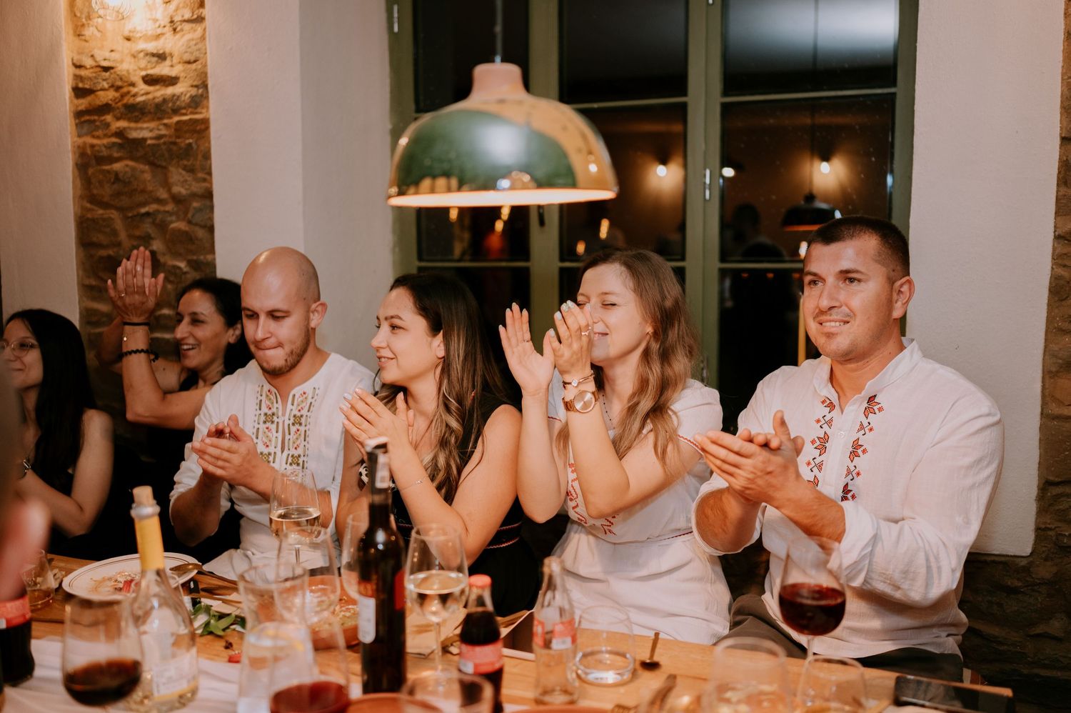 Dinner party guests enjoying conversation at tables in a warmly lit restaurant setting.