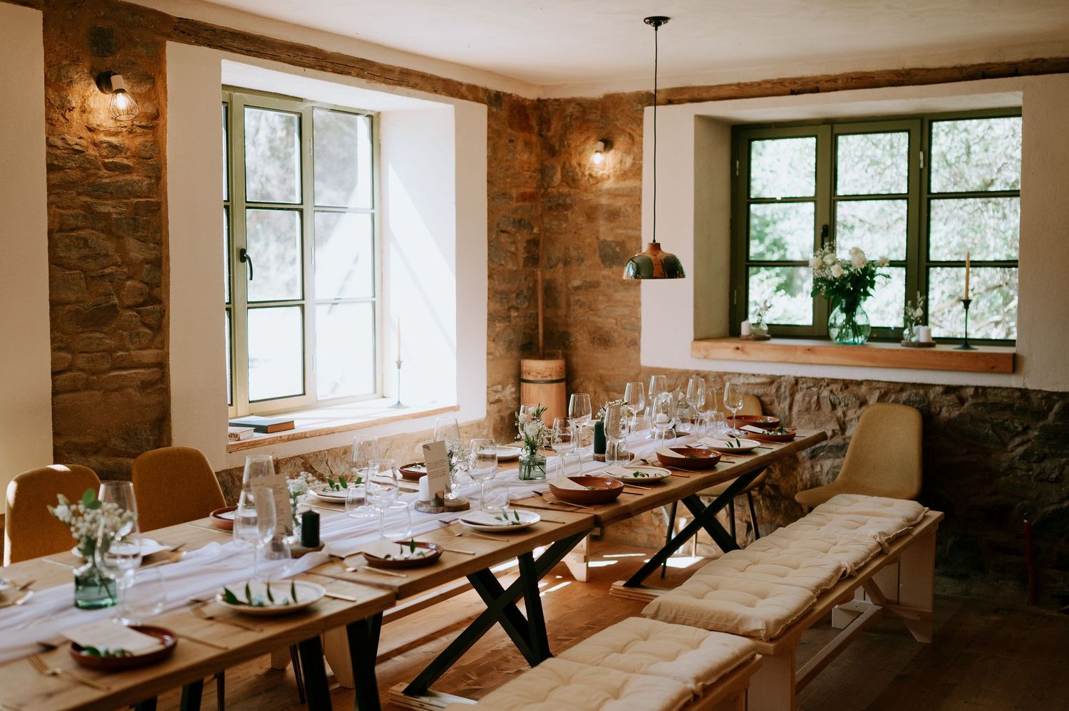 Rustic dining room with stone walls, wooden tables, and pendant lighting set for an elegant event.