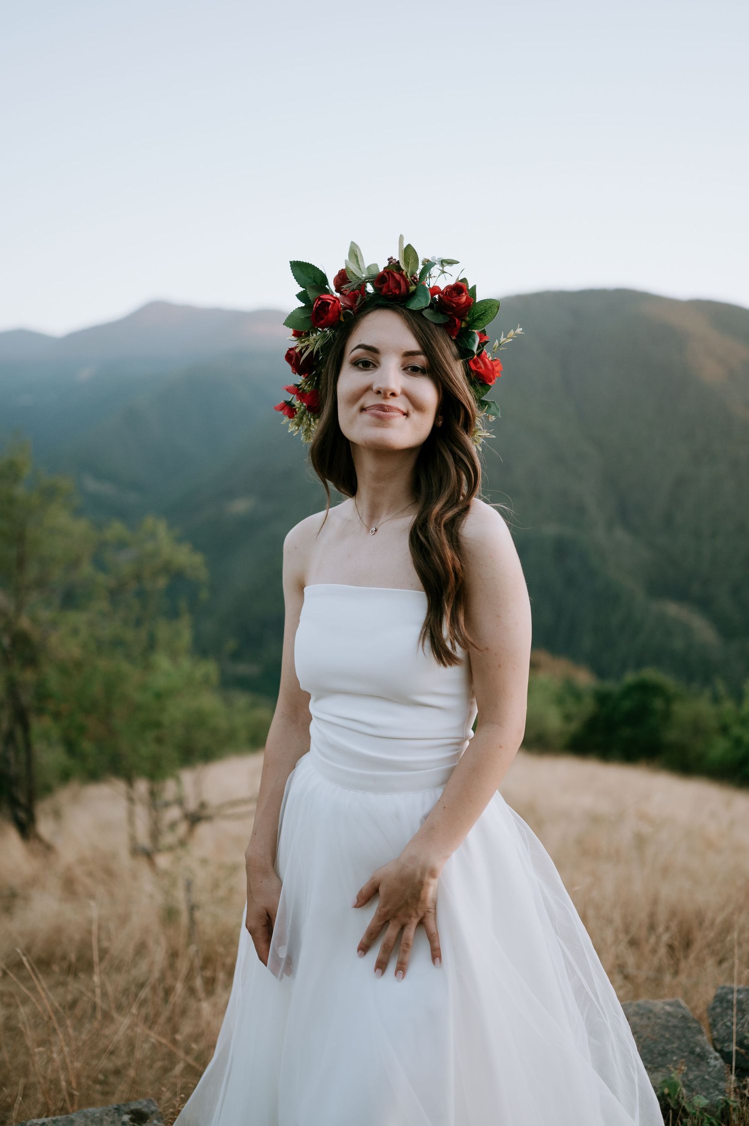 A white wedding dress flows in the breeze on a mountain overlook with dried grass.