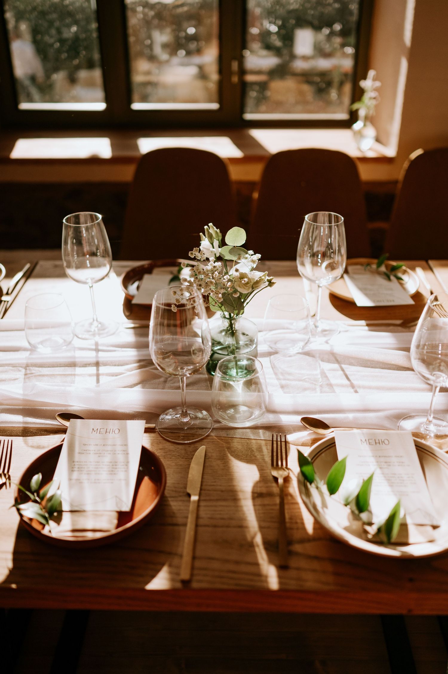 Elegant restaurant table setting with wine glasses and delicate floral centerpiece in natural light.
