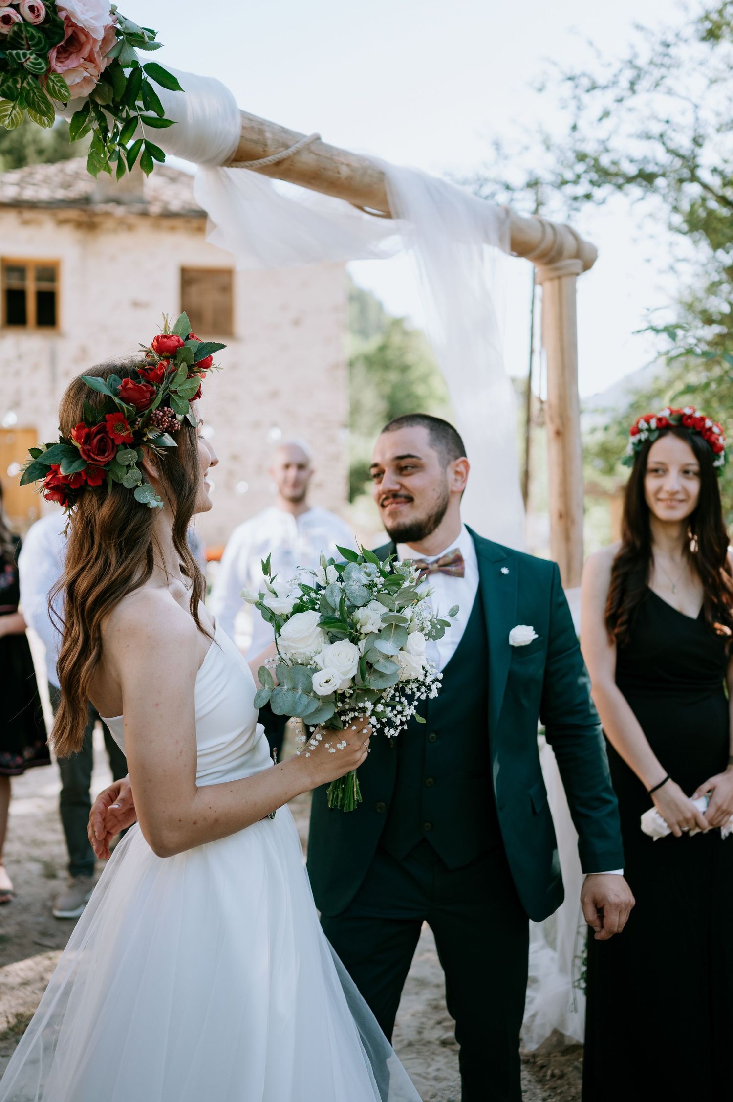 Wedding celebration in a rustic courtyard with white drapery and red floral accents.