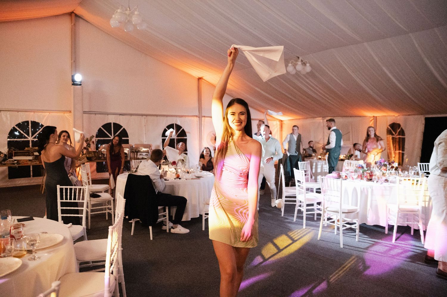 White wedding reception tent interior with elegant table settings and purple accent lighting creating a romantic atmosphere.