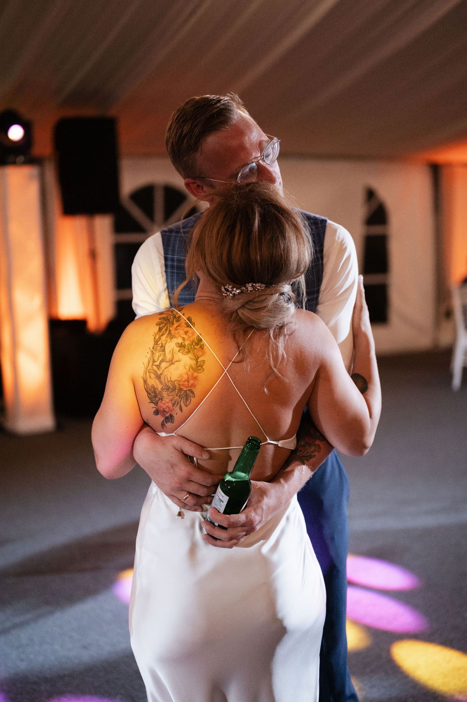 A couple shares an intimate dance moment in a dimly lit room with warm lighting and shadows.