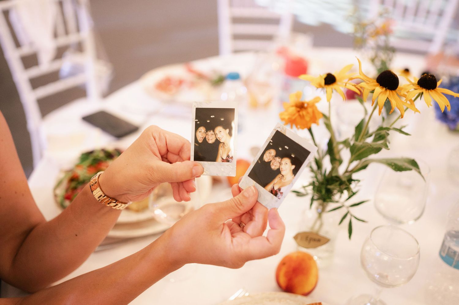 Hands arranging elegant table settings with floral centerpieces, peaches, and glassware for a special dining event.