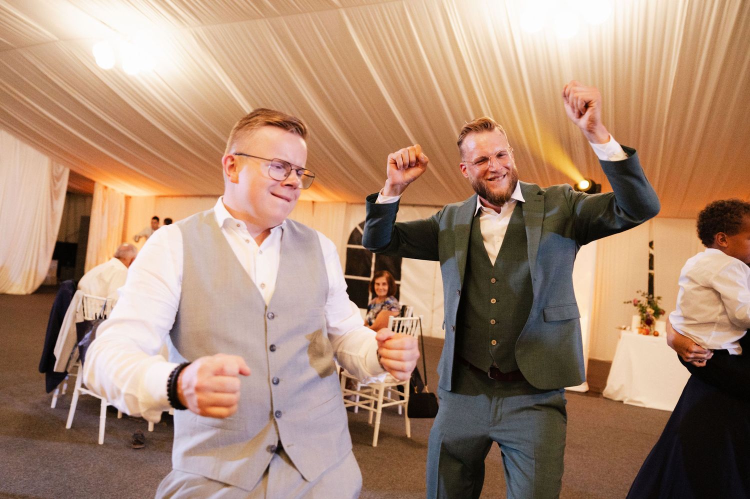 Wedding party members dancing and having fun during a reception celebration under draped tent lighting.