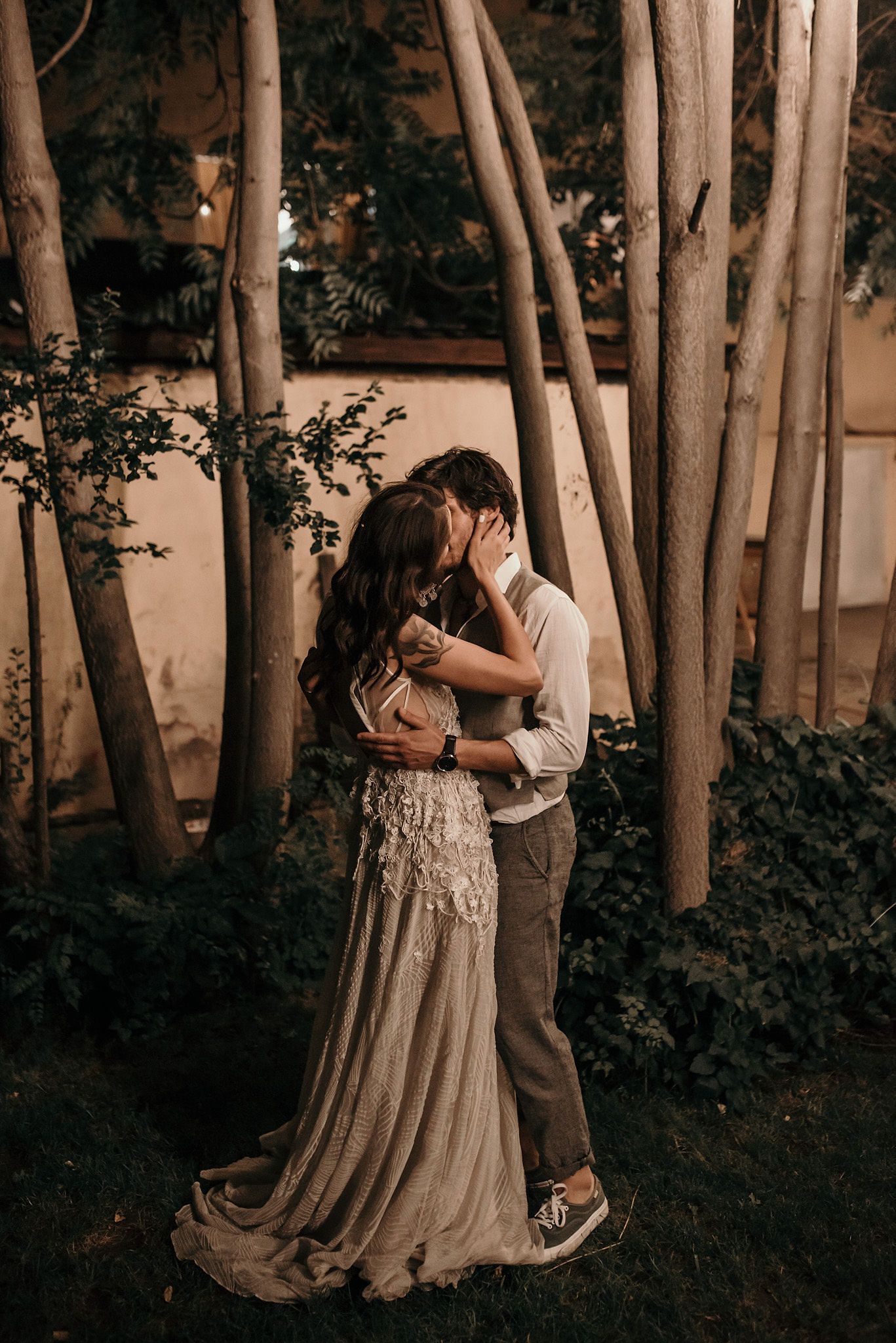 A romantic couple embraces among birch trees in a wooded garden setting at dusk.