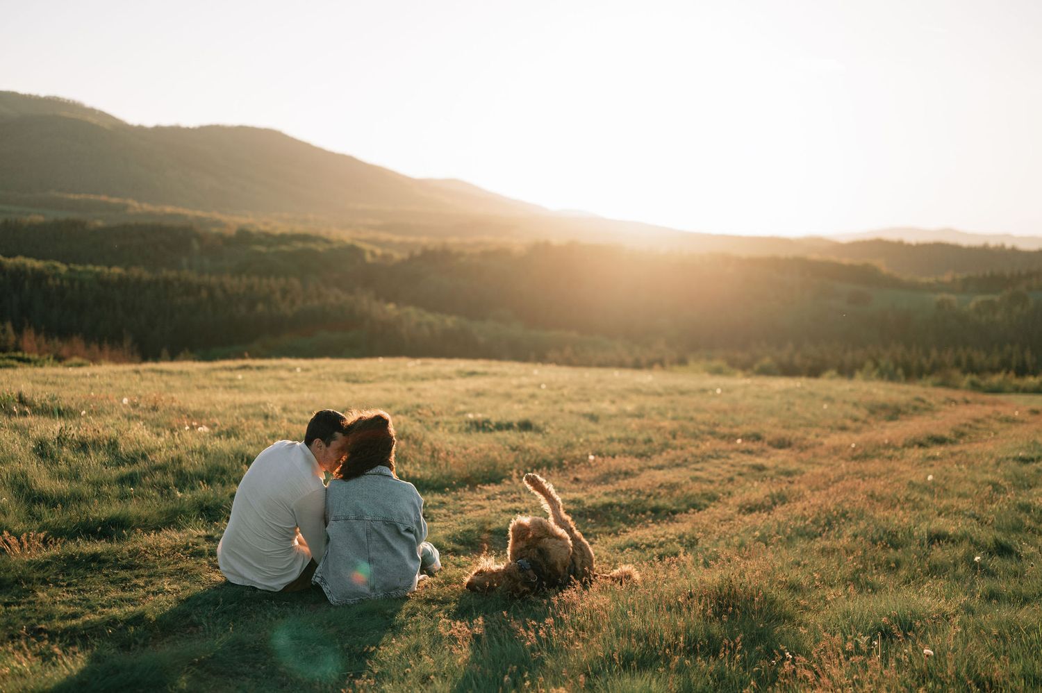 A scenic sunset view of rolling hills with two silhouettes sitting together in the distance.