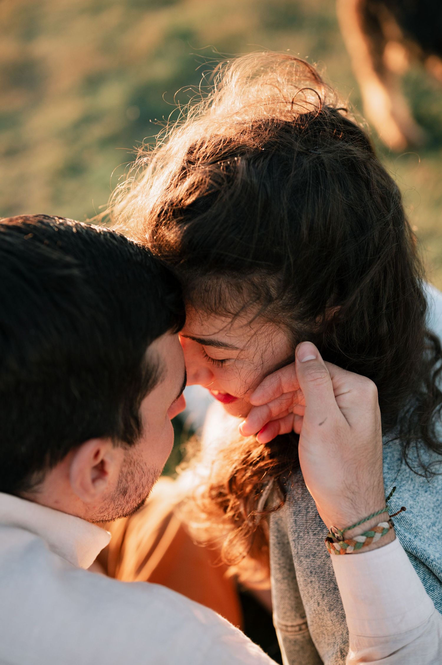A couple shares an intimate moment in golden sunlight against a blurred natural background.