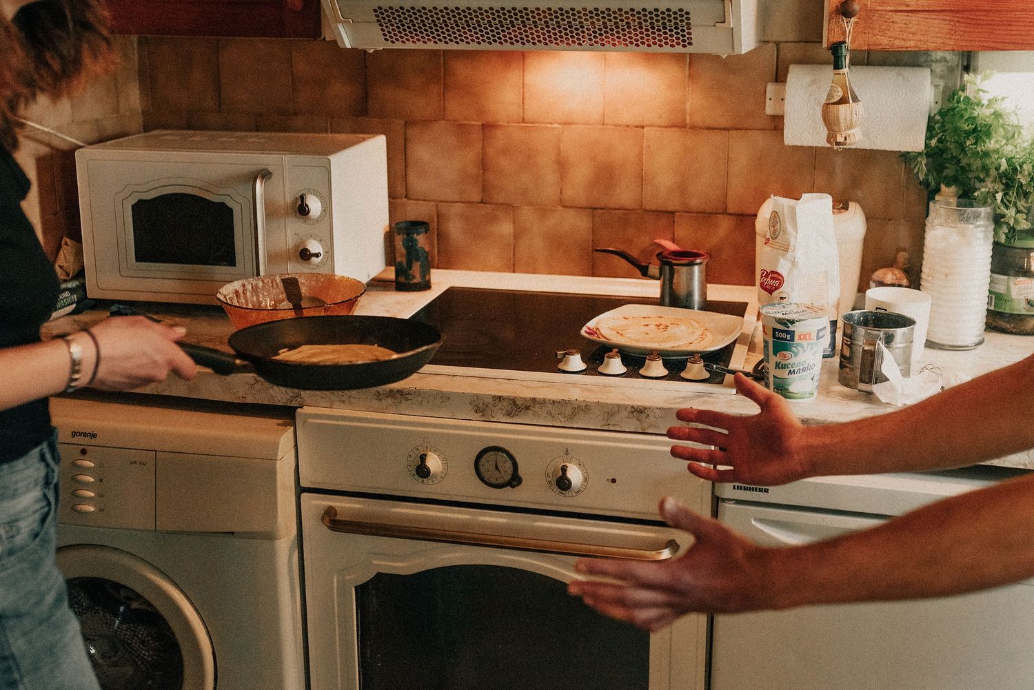 Two people cooking together in a modern kitchen with stainless steel appliances and warm lighting.