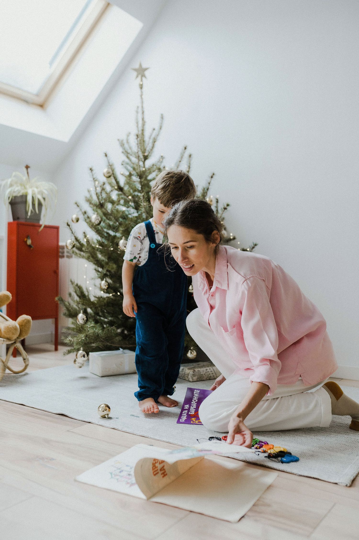 Two people decorating for Christmas with a tree and crafts in a bright room with a skylight.