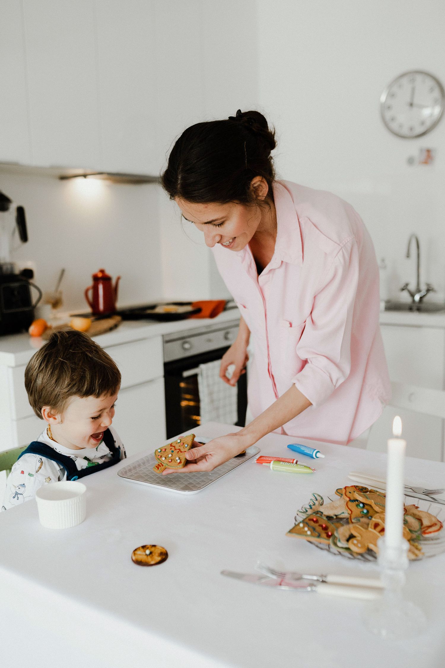 A parent and child baking cookies together in a bright white modern kitchen with natural lighting.