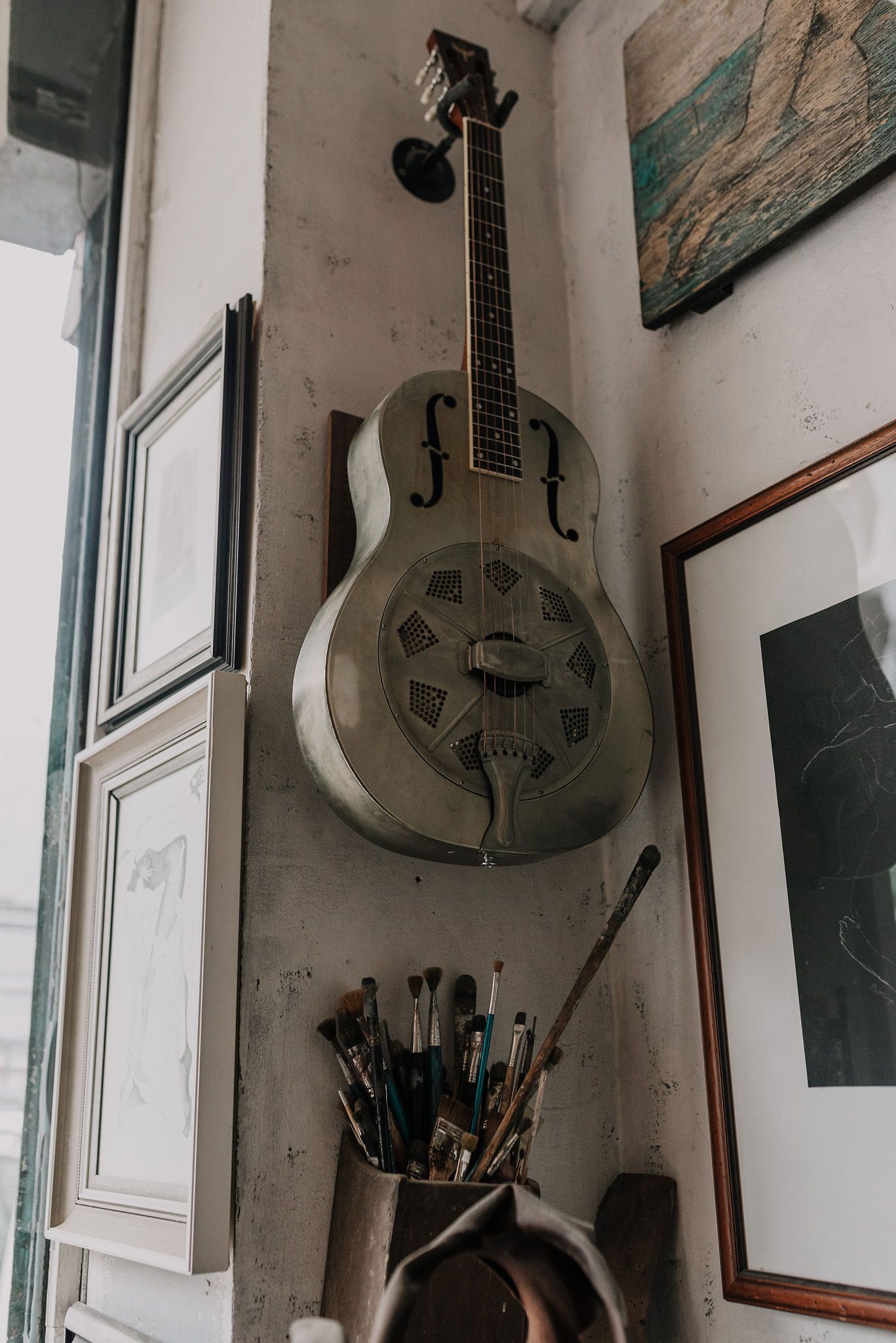 Metal guitars and art supplies displayed on white studio walls near windows.