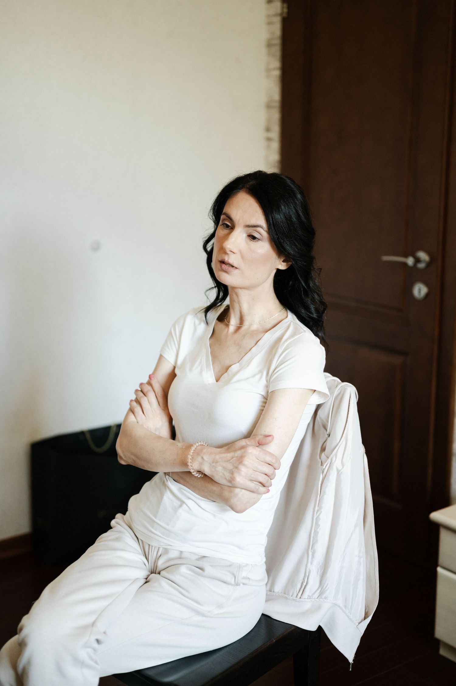 Woman in white silk robe sitting thoughtfully during wedding preparations.