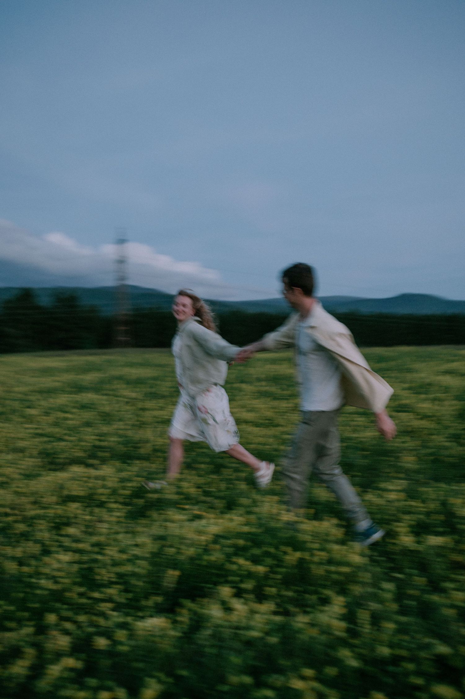 Couple spins joyfully through a yellow flower field on a summer evening.