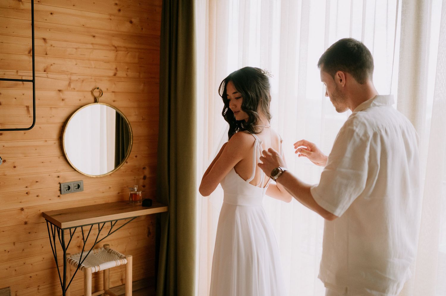 Bright sunlit room with white curtains and wooden wall panels.