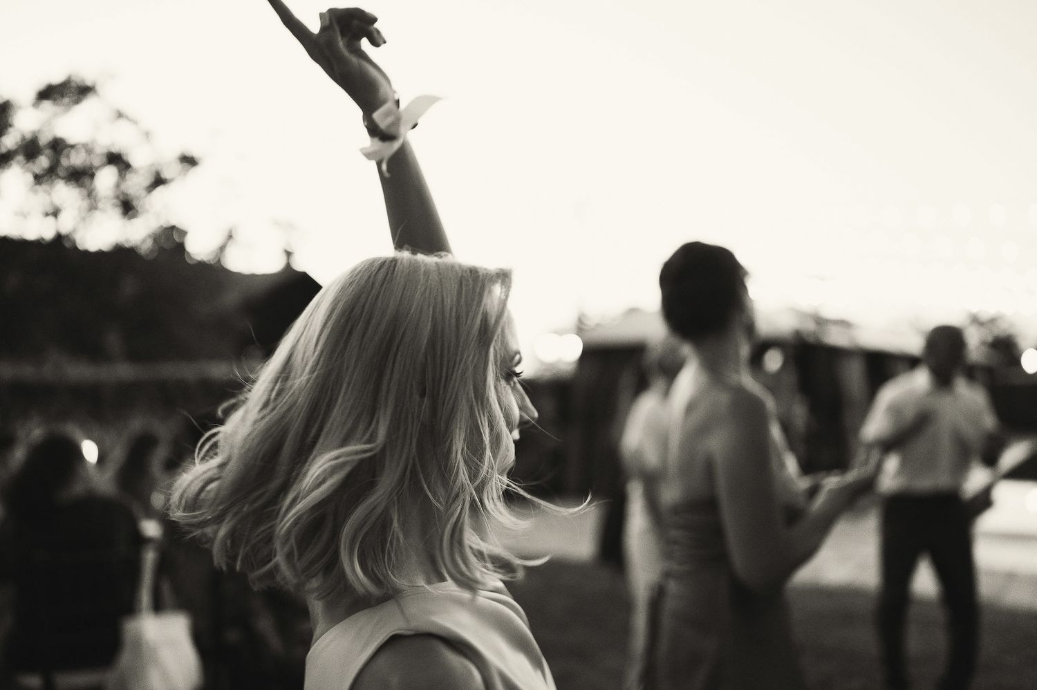 Silhouettes of party guests dancing against a sunset sky with string lights overhead.
