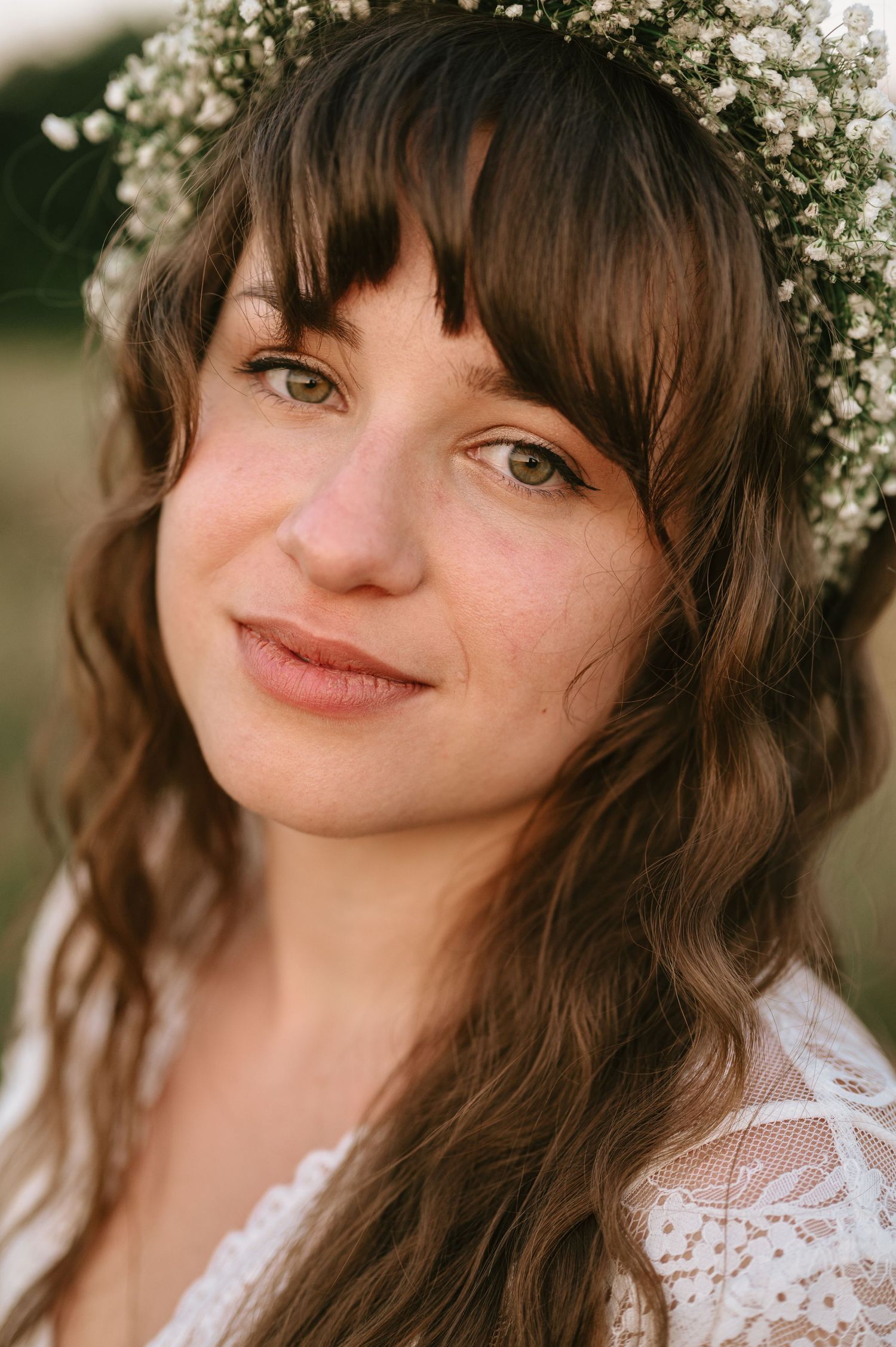 A delicate baby's breath flower crown adorns long brown wavy hair against a soft natural background.