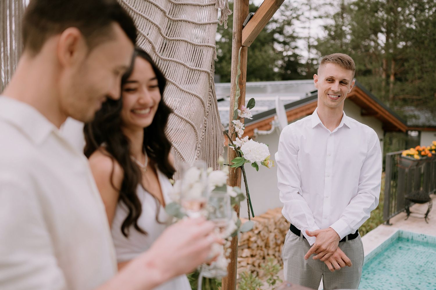 Outdoor venue decorated with white florals and wooden beams near a swimming pool.