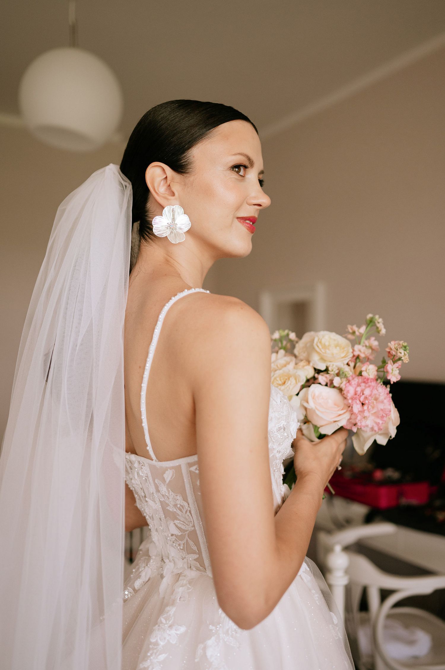 Side profile of bride in white gown with flowing veil holding romantic floral bouquet.