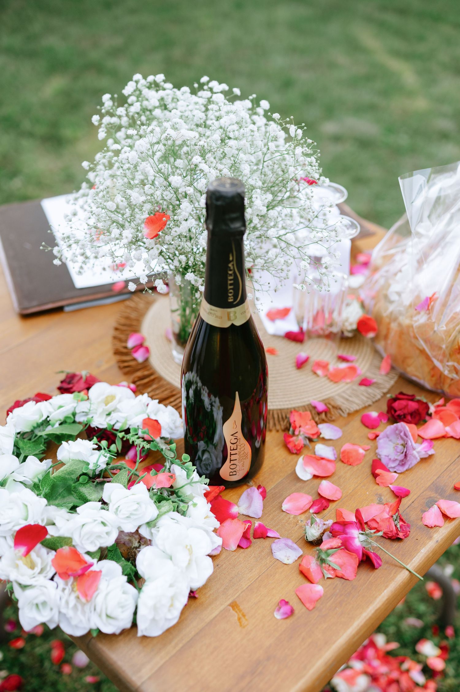 Table setting with champagne bottle, white flowers and scattered pink rose petals.