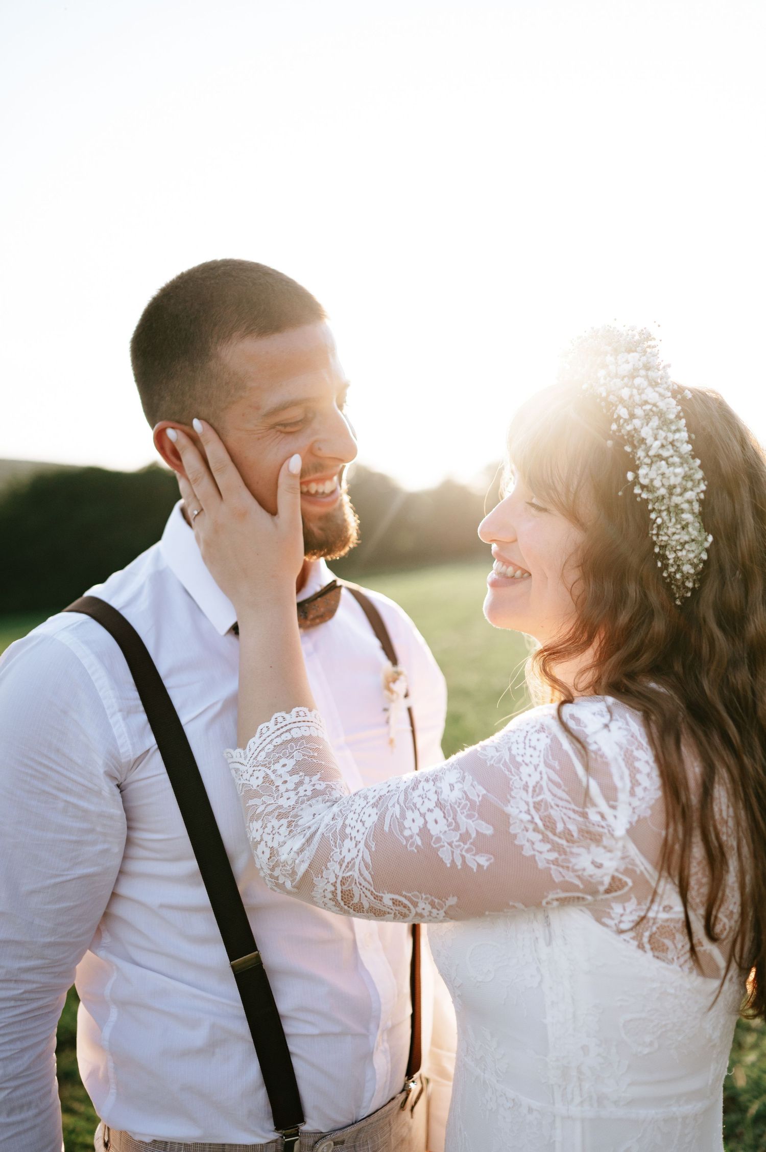 Sunset wedding portrait captures tender moment between laughing couple in field.