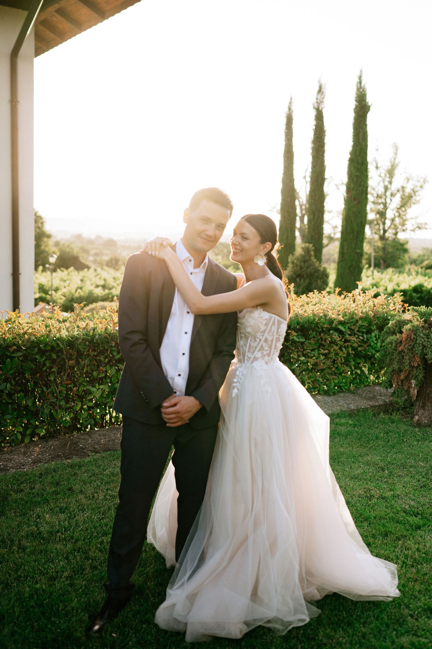 Elegant couple shares a joyful dance moment on their wedding day with garden scenery at sunset.
